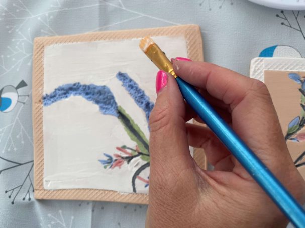 a lady painting a handmade floral coaster using brightly coloured glazes 