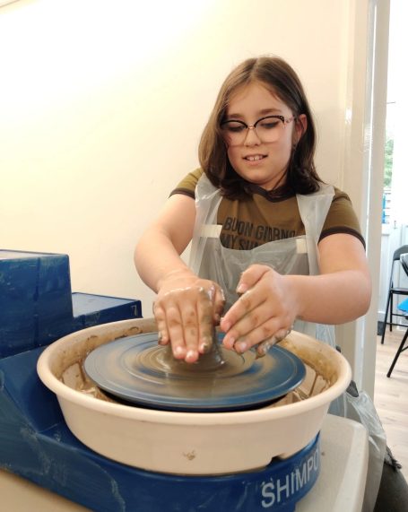 a young lady throwing a pot on the potters wheel