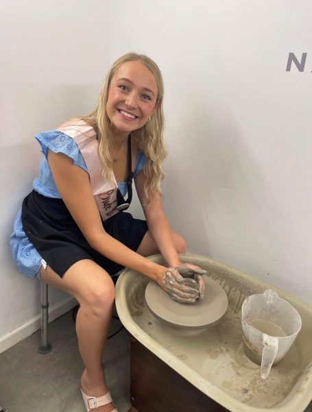 a lady smiling whilst throwing a pot on the potters wheel