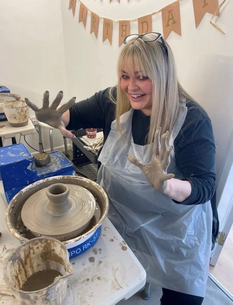 a lady holding her messy hands up whilst on the potters wheel